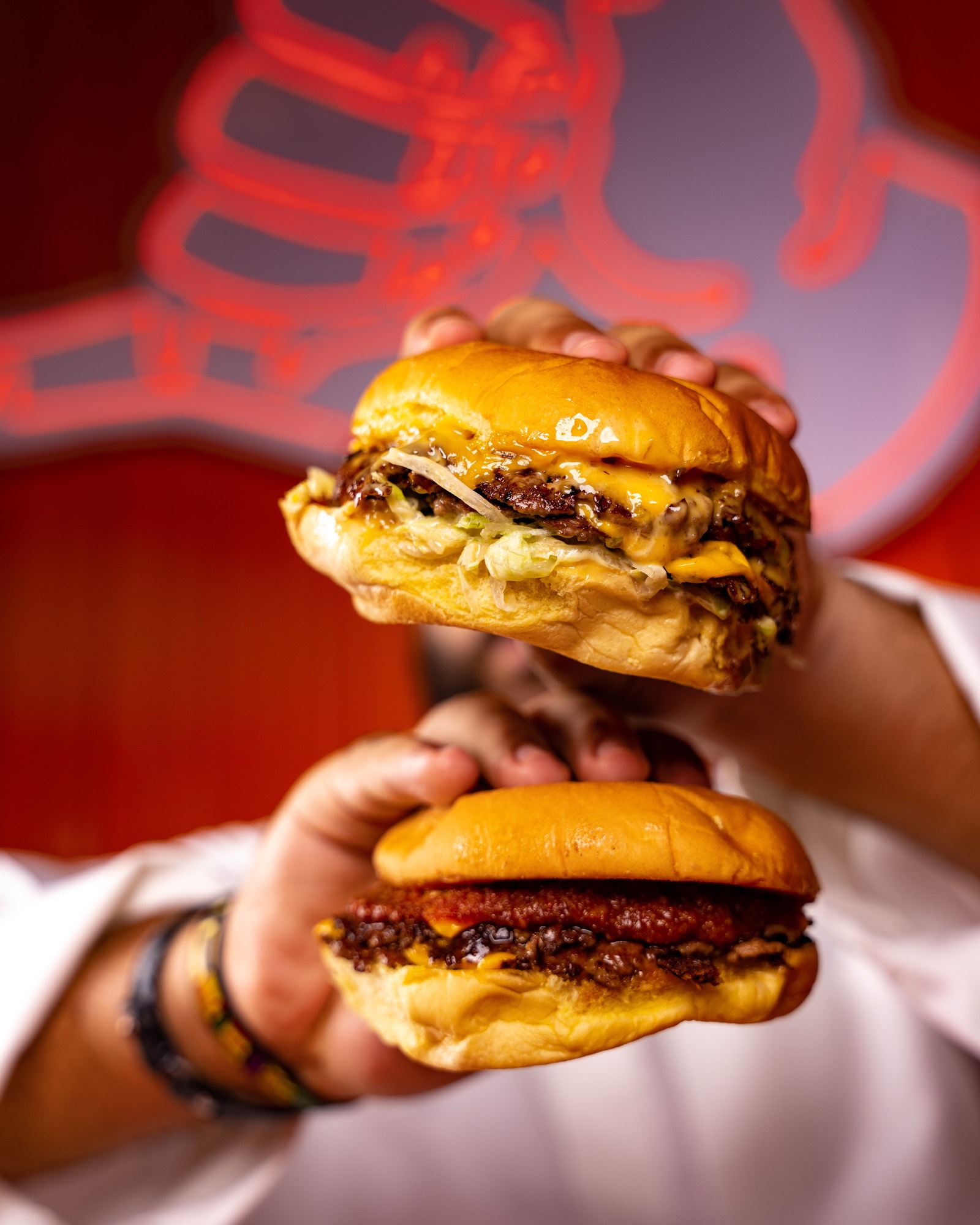 Two JAMZ smash burgers held up in front of the neon sign, cheese melting over the patties